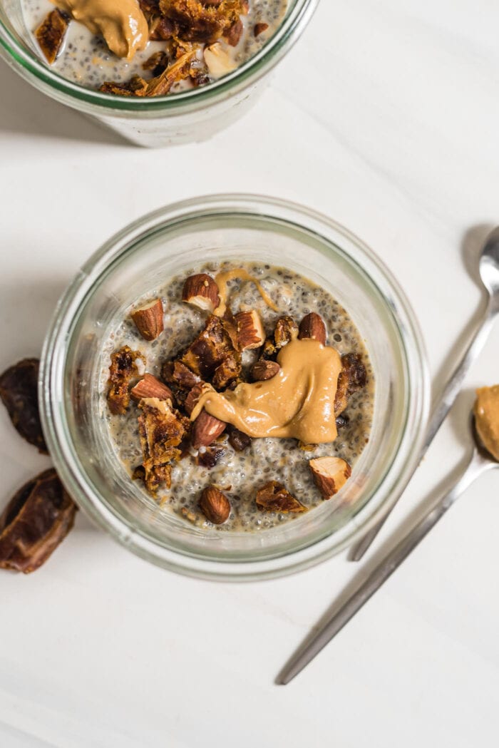Overhead view of a jar of chia seed pudding topped with chopped nuts, dates and peanut butter.