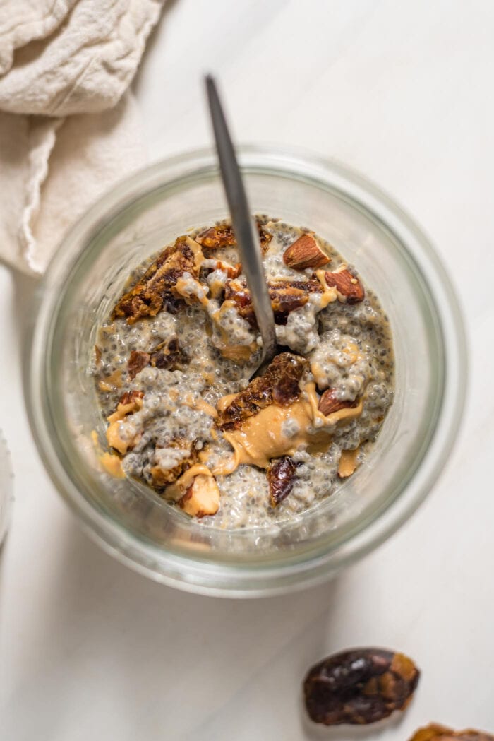 Overhead view into a jar of chia seed pudding with peanut butter, dates and almonds.