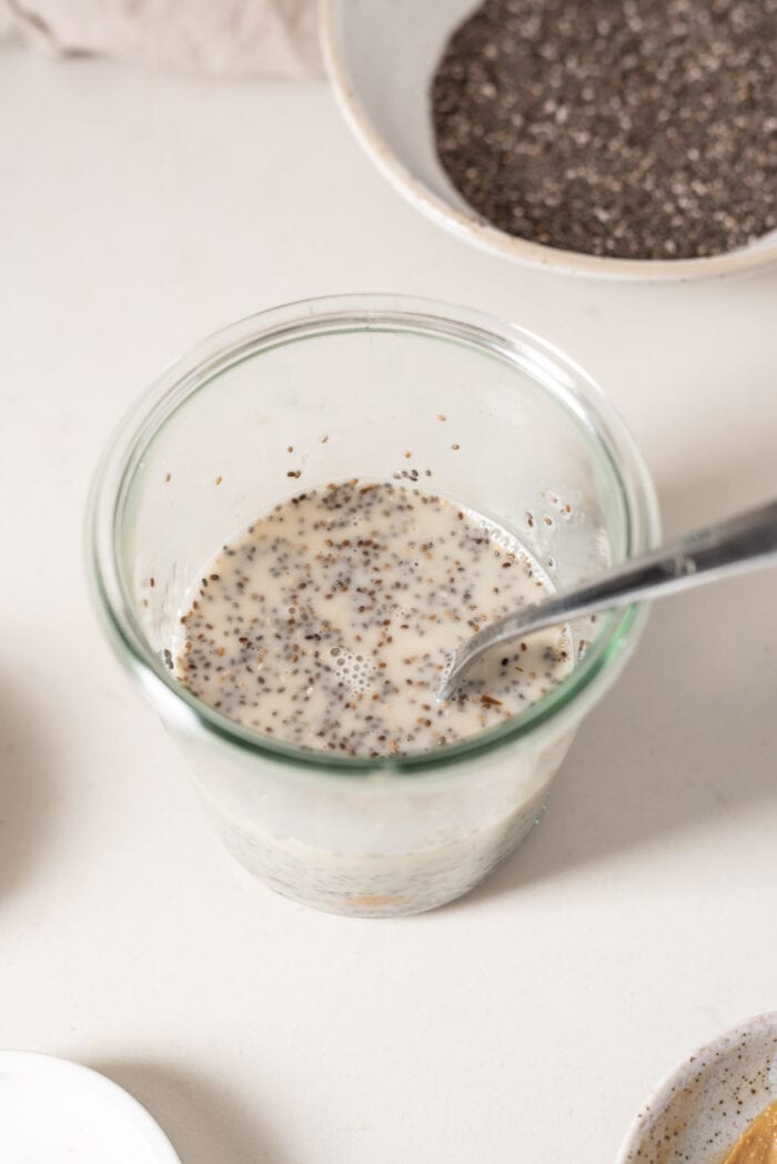 Chia seeds mixed into milk in a jar with a spoon.