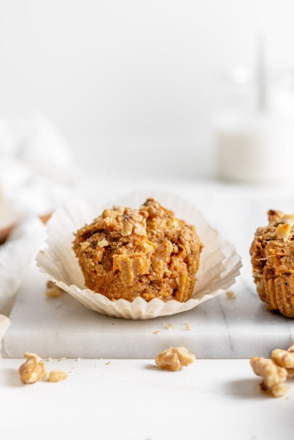 Small carrot muffin in a cupcake liner sitting on a marble cutting board.