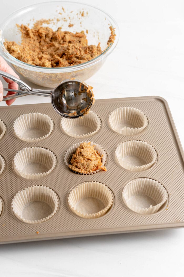 Scooping raw muffin batter into muffin liners in a muffin pan.