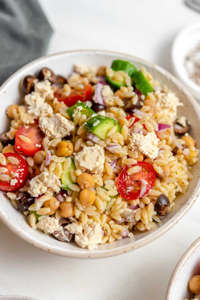 Close up of a bowl of Mediterranean orzo salad with tomato, cucumber and olives.