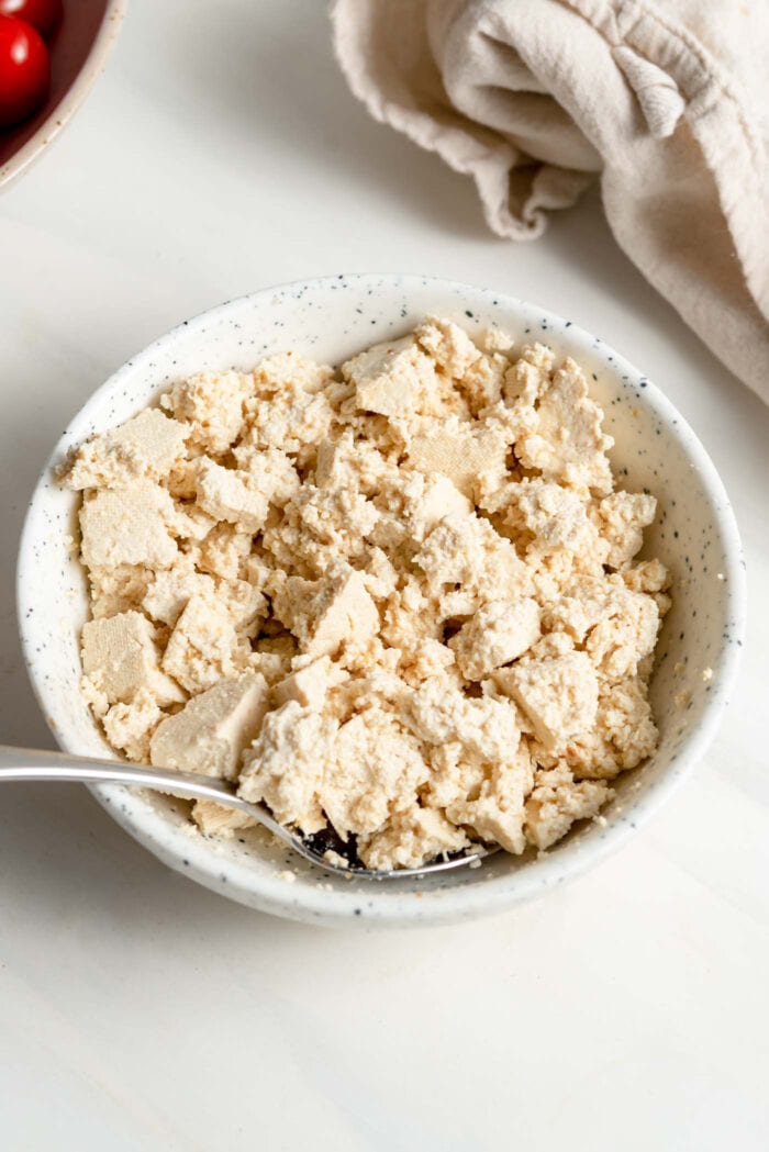 Crumbled tofu in a small bowl with a spoon.