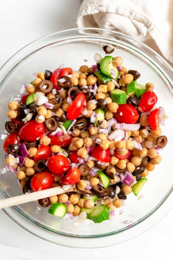 Chopped tomato, cucumber, olives, onion and chickpeas in a glass mixing bowl.