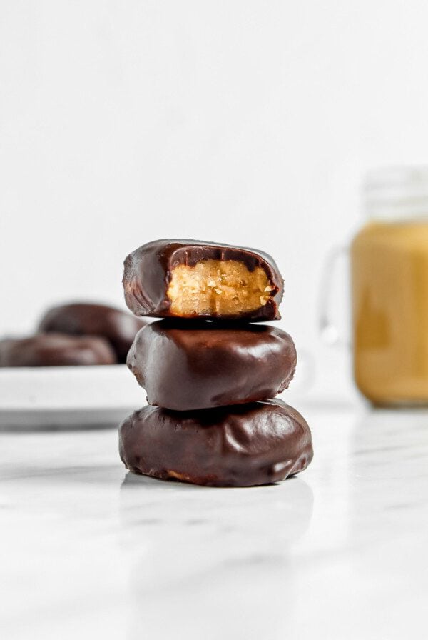 Stack of 3 peanut butter eggs on a marble surface, one on top has a bite out of it showing peanut butter filling.