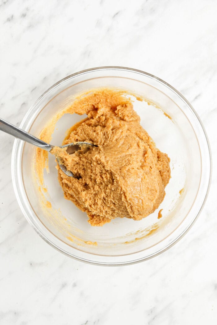 Thick peanut butter batter in a mixing bowl with a spoon.