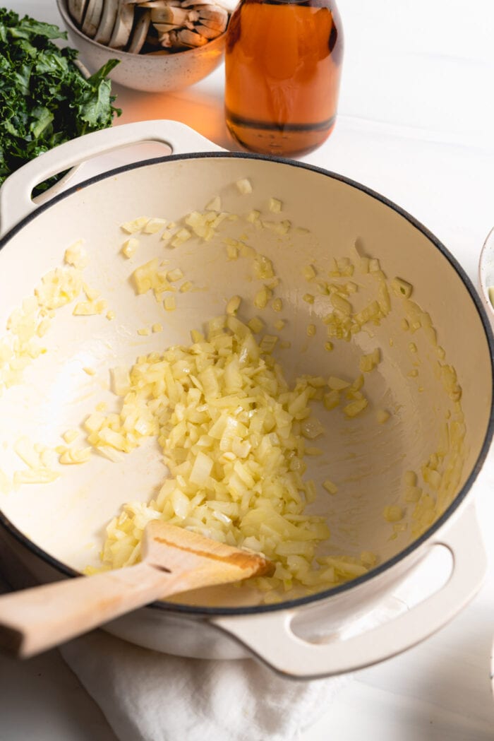 Chopped onions and garlic cooking in a large pot with a wooden spoon.