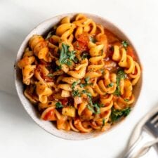 Overhead view of a bowl of rotini pasta with tomato sauce and vegetables.