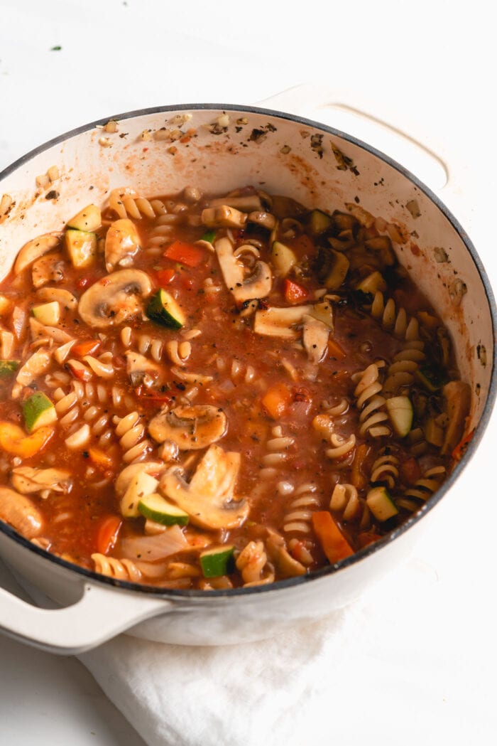 Rotini and vegetables cooking in tomato sauce in a pot.