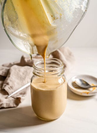 Pouring a peanut butter smoothie from a blender into a jar.