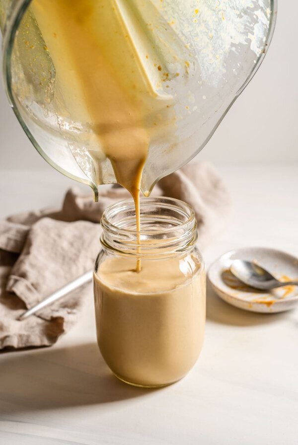 Pouring a peanut butter smoothie from a blender into a jar.