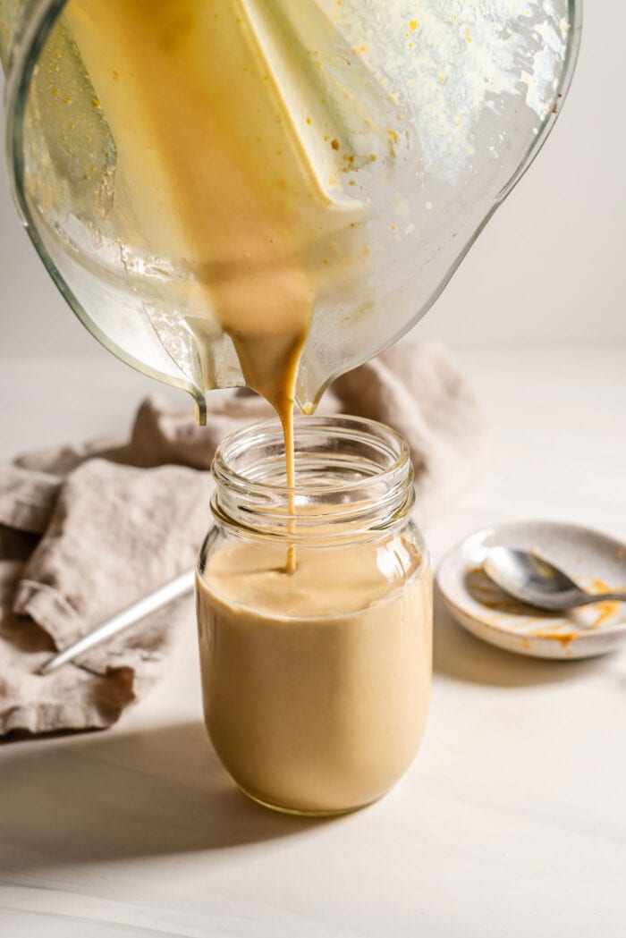 Pouring a peanut butter smoothie from a blender into a jar.