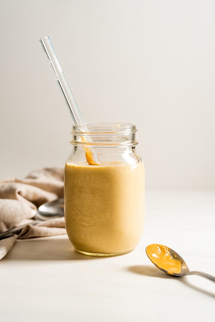 Peanut butter protein shake in a jar with a straw. Spoon rests beside jar.