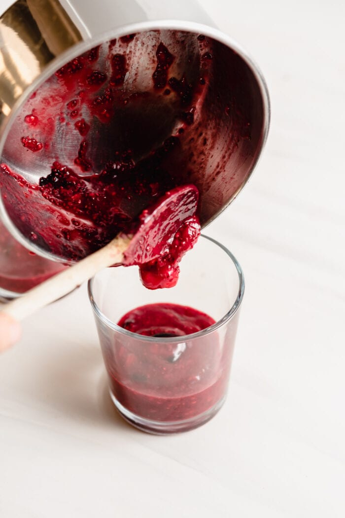 Pouring a berry compote from a pot into a small jar.