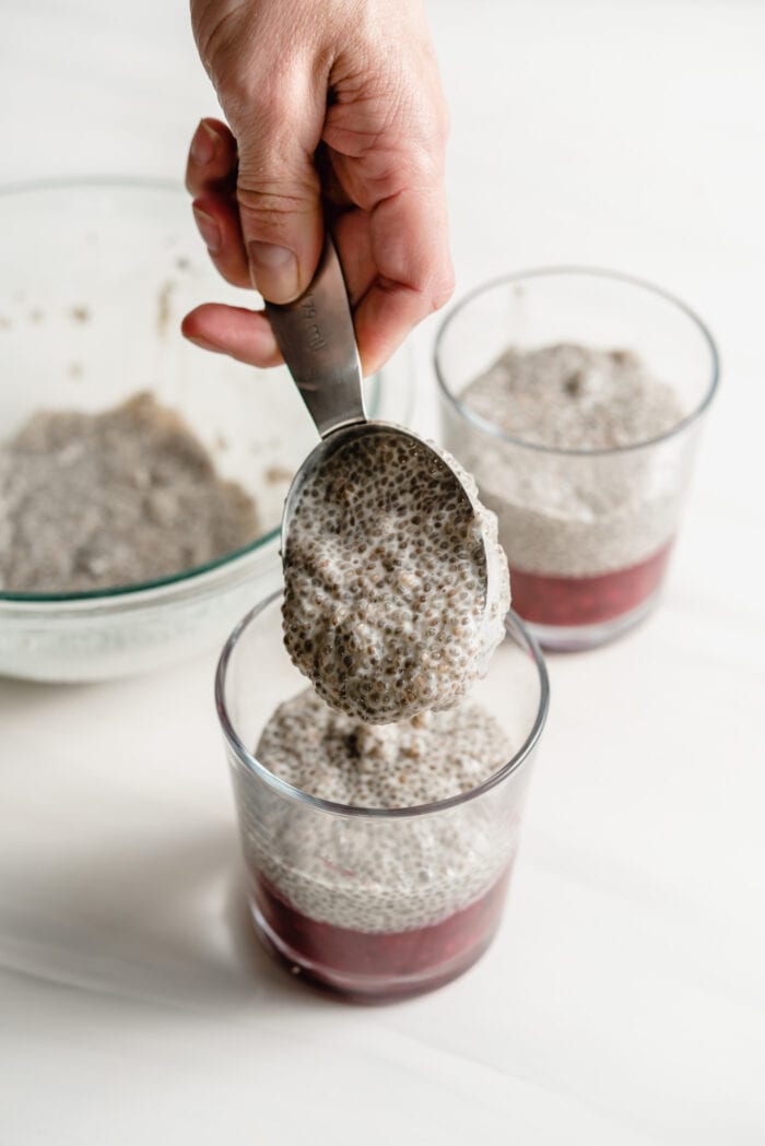 Adding a scoop of chia pudding to berry compote in small glass jars.