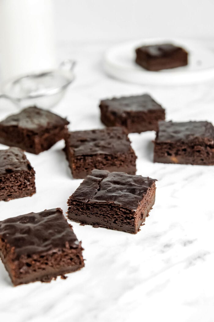 A number of squares of chocolate vegan sweet potato brownies sitting on a marble surface.