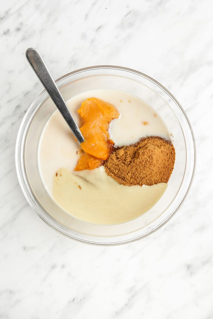 Mashed sweet potato, sugar, milk and almond butter in a large glass mixing bowl with a spoon.