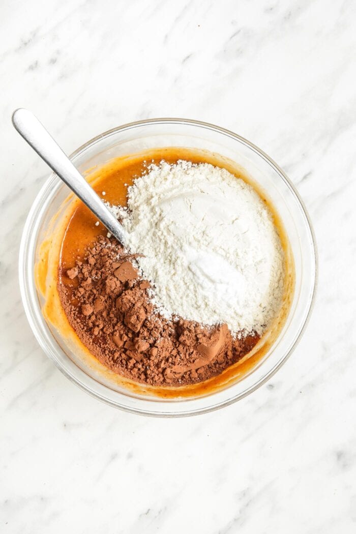 Flour and cocoa powder added to a mixing bowl of raw batter.