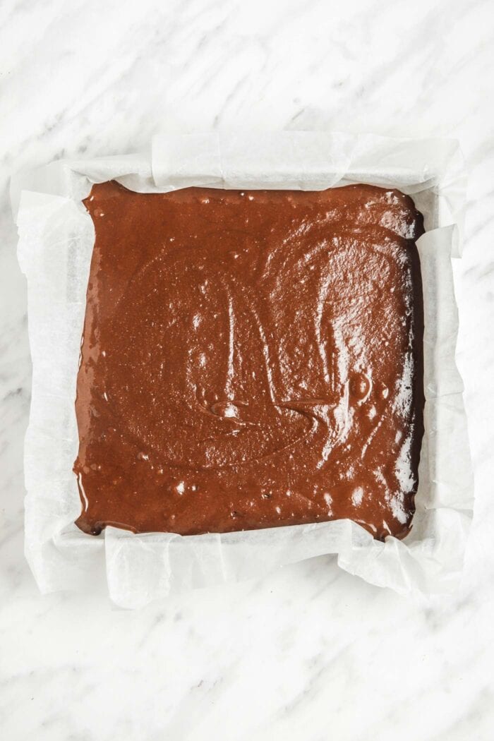 Raw sweet potato chocolate chip brownie batter in a baking tray lined with parchment paper.