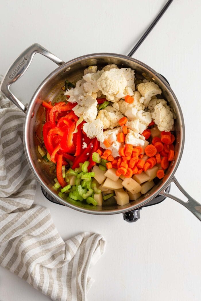 Bell pepper, cauliflower, potato and celery cooking in a large metal pan.