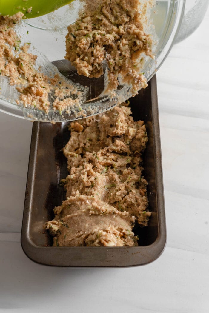 Scooping raw zucchini bread batter into a loaf pan.