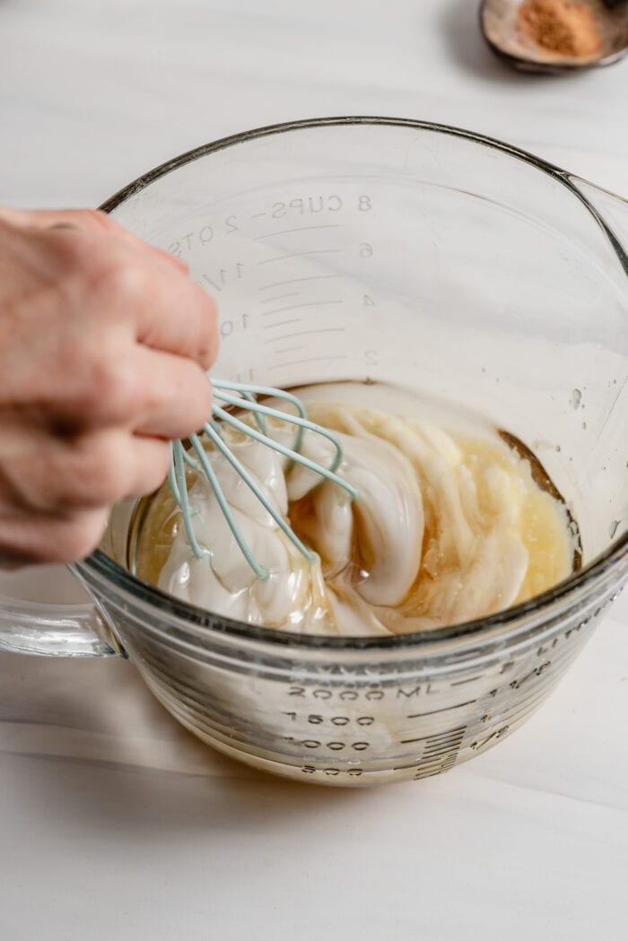 Whisking coconut oil and yogurt together in a large glass mixing bowl.