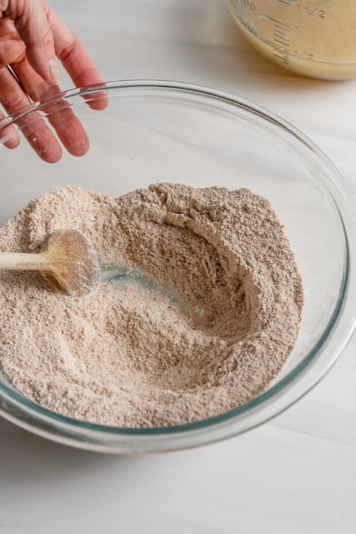 Wooden spoon mixing flour in a glass mixing bowl.