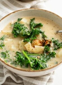 Two bowls of vegan zuppa toscana soup with potato and kale. Spoon rests in bowl.