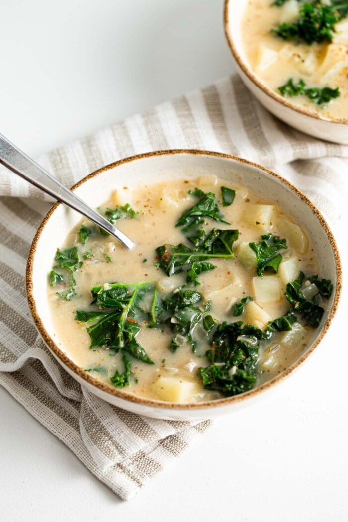 A bowl of zuppa Toscana soup with kale and potato sitting on a dish cloth on a counter top.