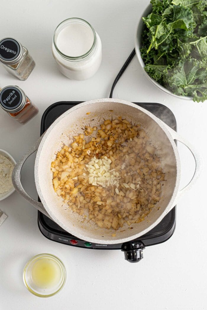 Onions and garlic cooking in a pot surrounded by small bowls of lemon juice, milk and kale.