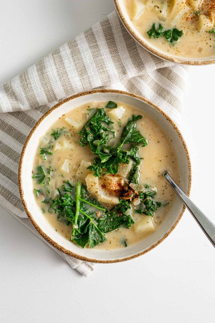 Overhead view of a bowl of creamy zuppa Toscana soup with kale and potatoes with a spoon in the bowl.
