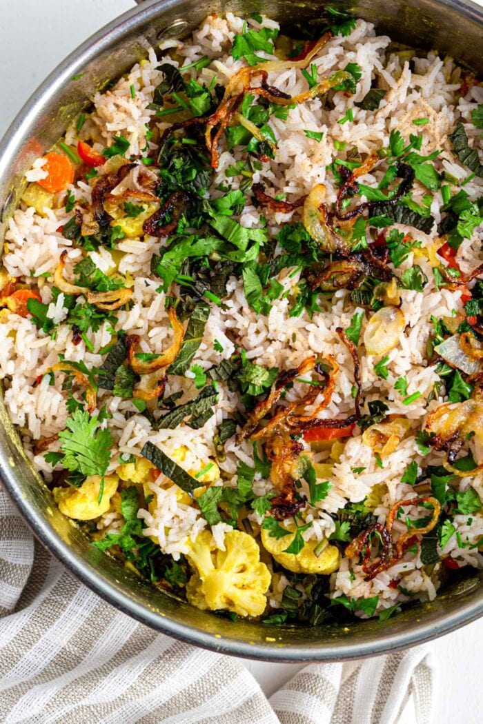 Overhead view of vegetable biryani topped with onions and herbs in a pot.