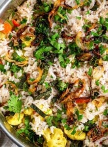 Overhead view of vegetable biryani topped with onions and herbs in a pot.