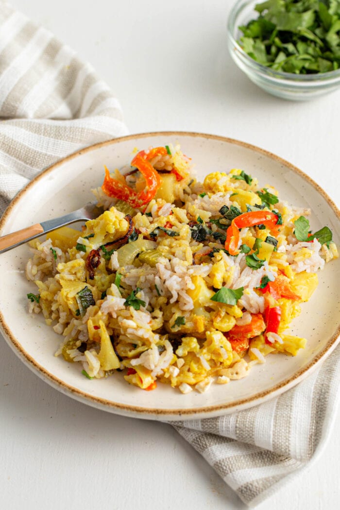 Vegan vegetable rice biryani with onions, potato and peppers on a plate with a fork.