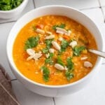 Bowl of mulligatawny soup topped with fresh herbs and peanuts.