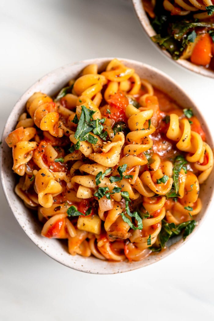 Overhead view of a bowl of rotini pasta with tomato sauce and vegetables.