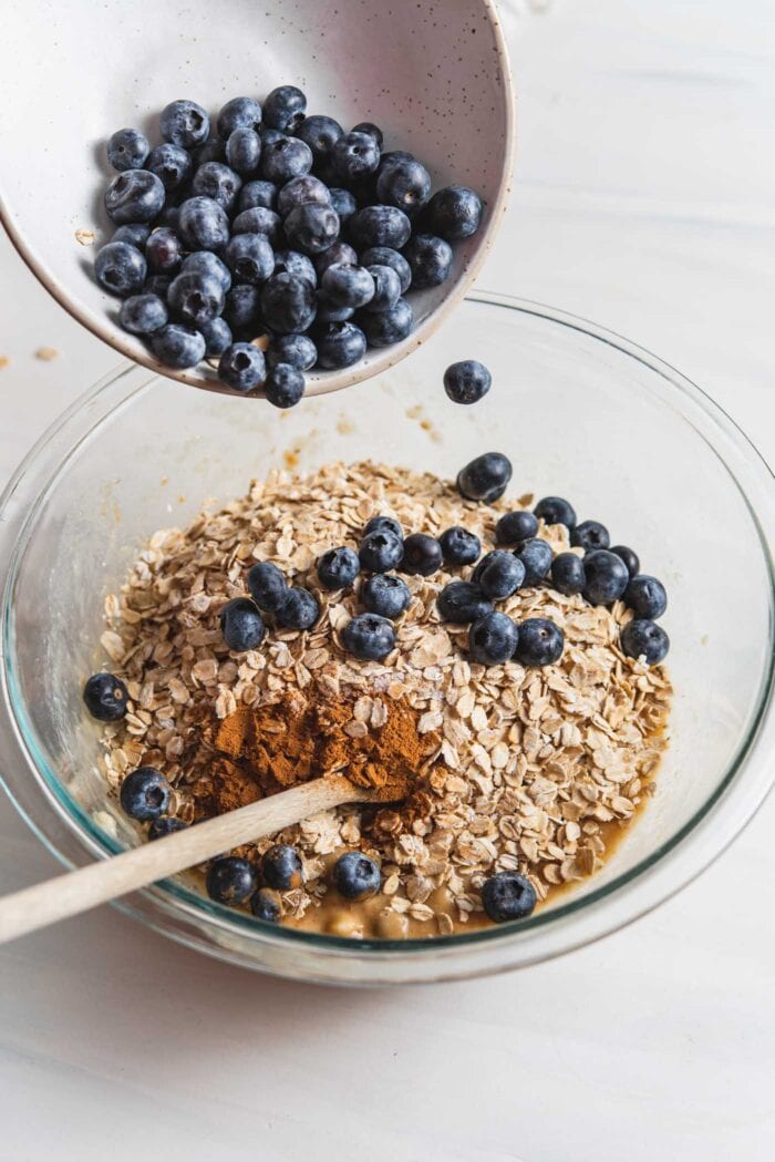 Adding blueberries to a bowl of mashed banana and oats.