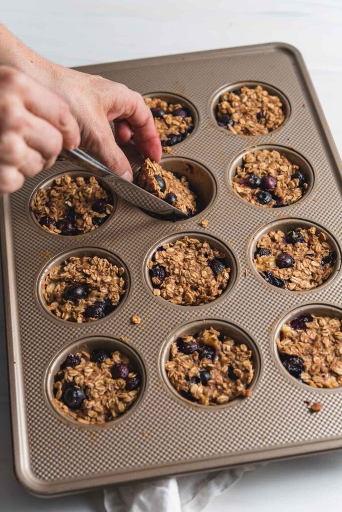 Hand using a knife to remove an oatmeal muffing from a 12-cup muffin pan.