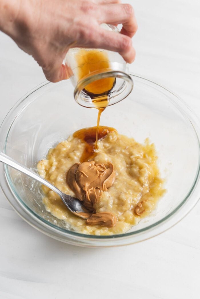 Hand pouring maple syrup into a bowl of mashed banana.