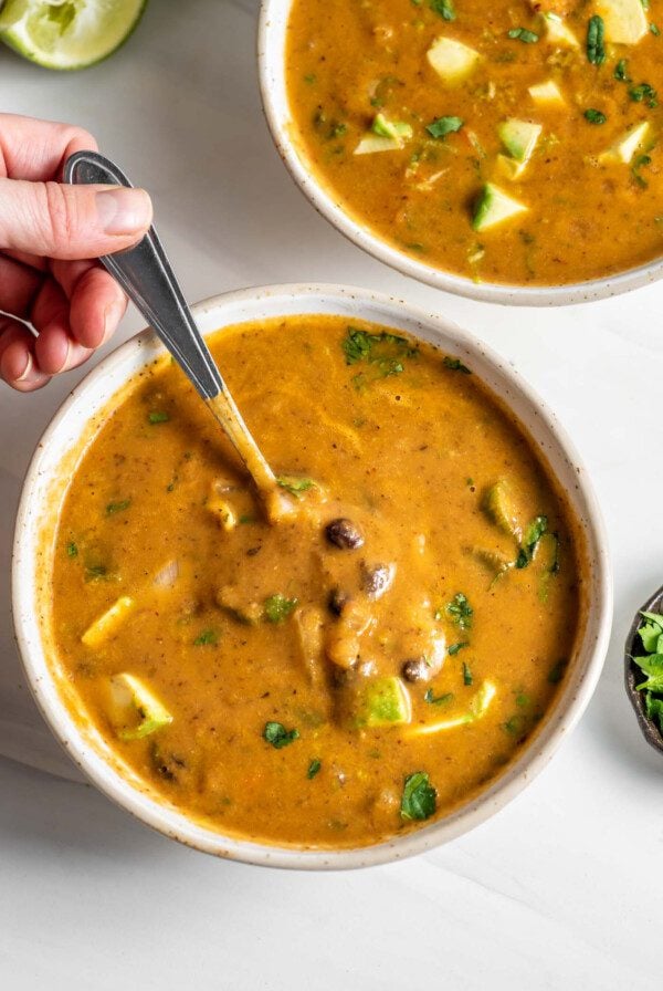 Hand using a spoon in a bowl of black bean vegetable soup.