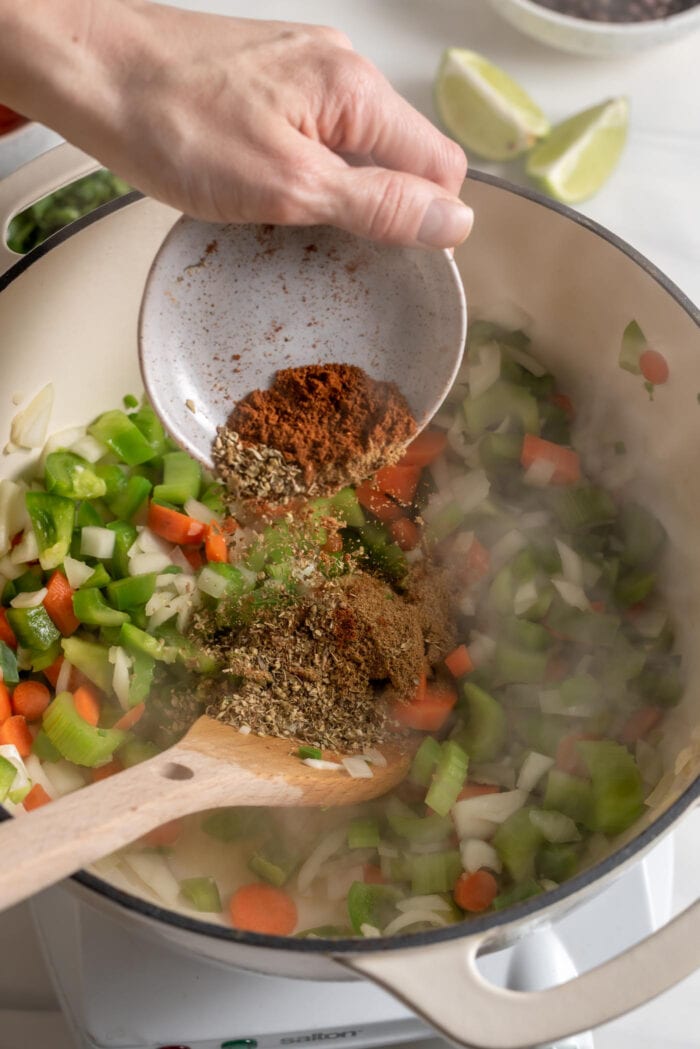 Add a small bowl of spices to a chopped vegetables cooking in a pot.