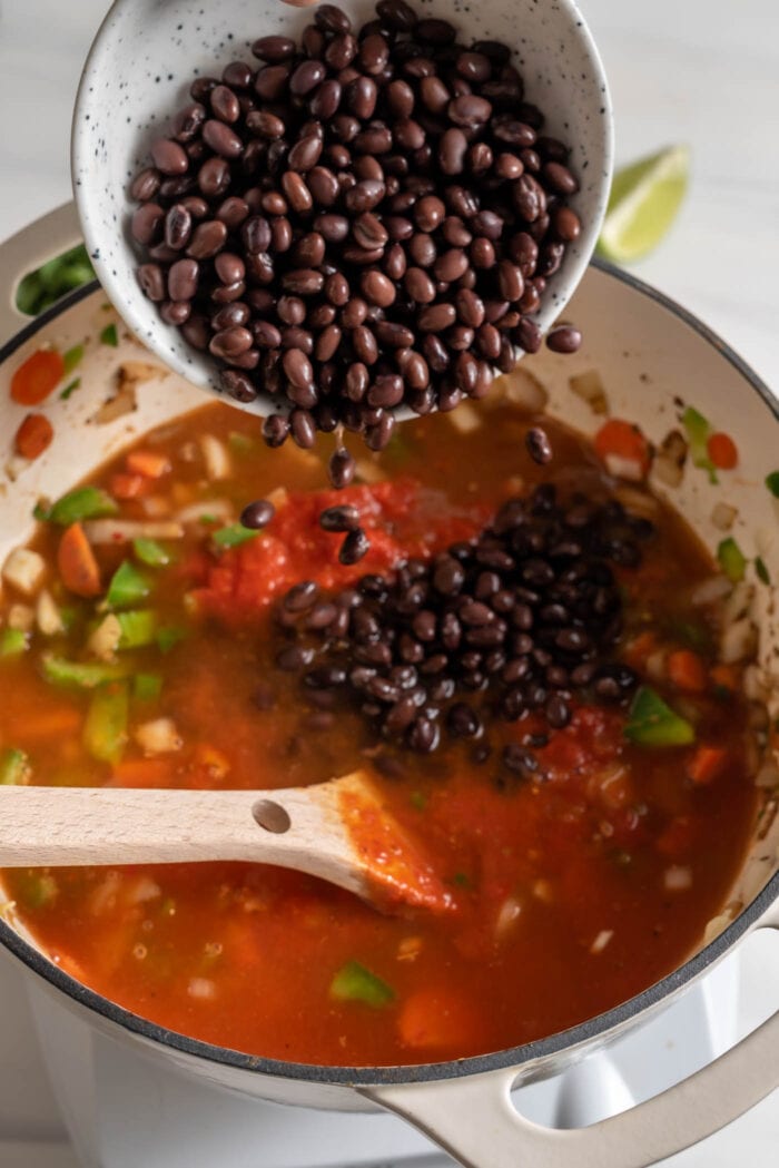 Dumping a bowl of black beans into a pot of tomato-based soup.