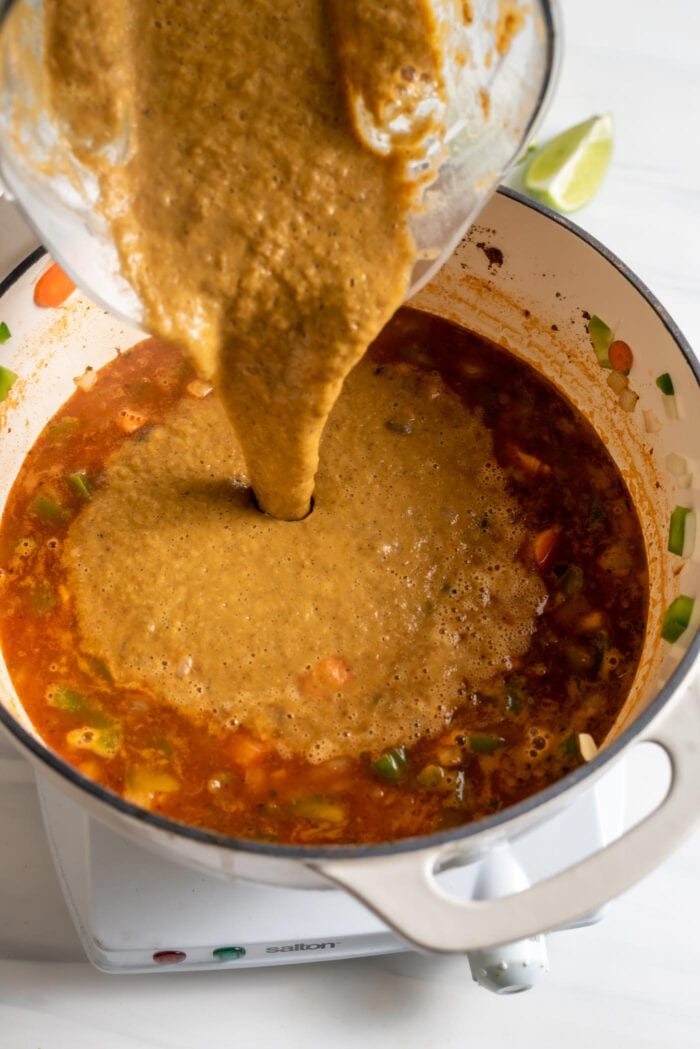 Pouring blended soup from a blender into a pot of vegetable tomato soup.