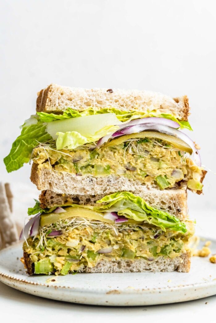 Two halves of a chickpea sandwich with sprouts and lettuce stacked on top of each other.