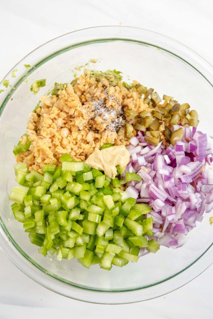 Chickpeas, celery, red onion, pickles and dijon mustard in a glass mixing bowl.