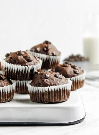 A number of chocolate muffins with chocolate chips in them sitting on a flipped over baking pan on a marble surface.