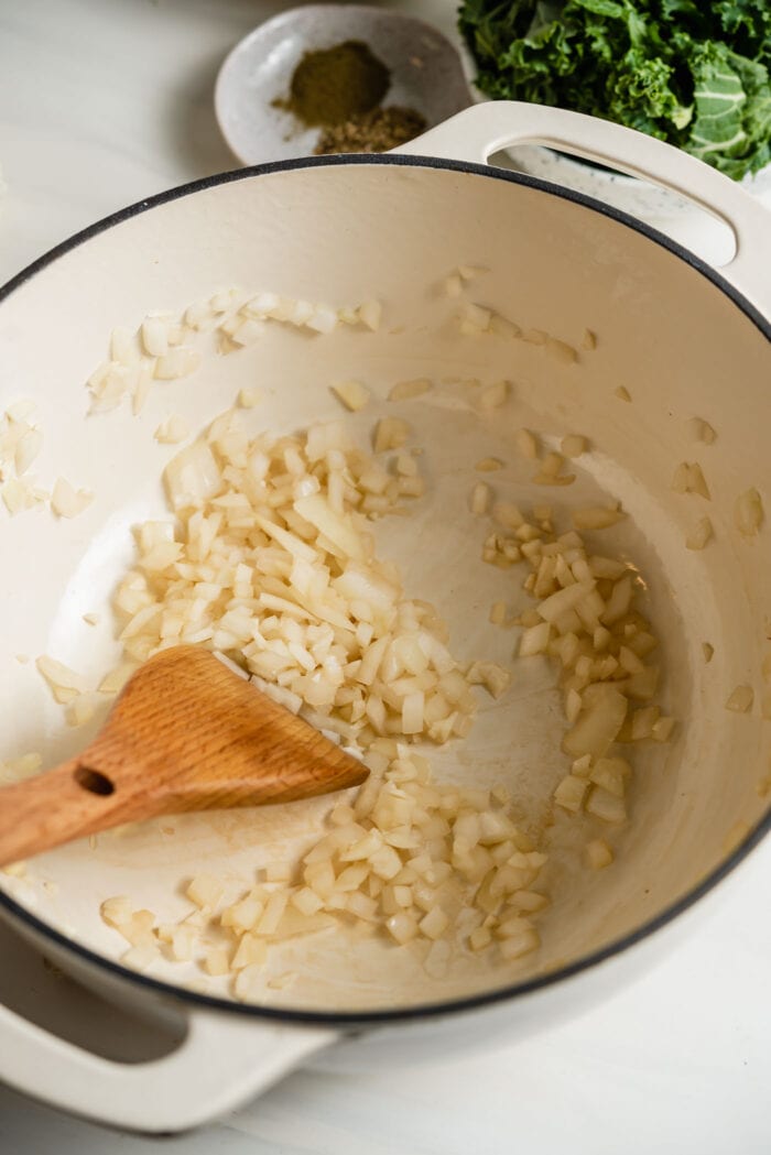 Sautéing chopped onion and garlic in a large soup pot with a wooden spoon.