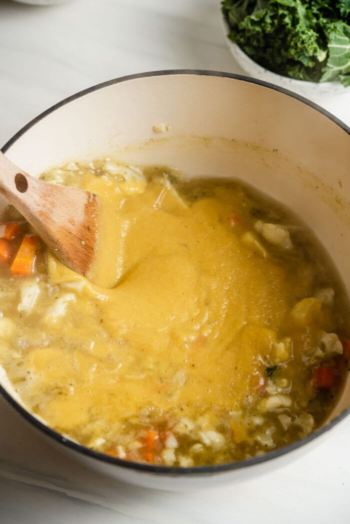 Stirring vegetable soup in a pot with a wooden spoon.