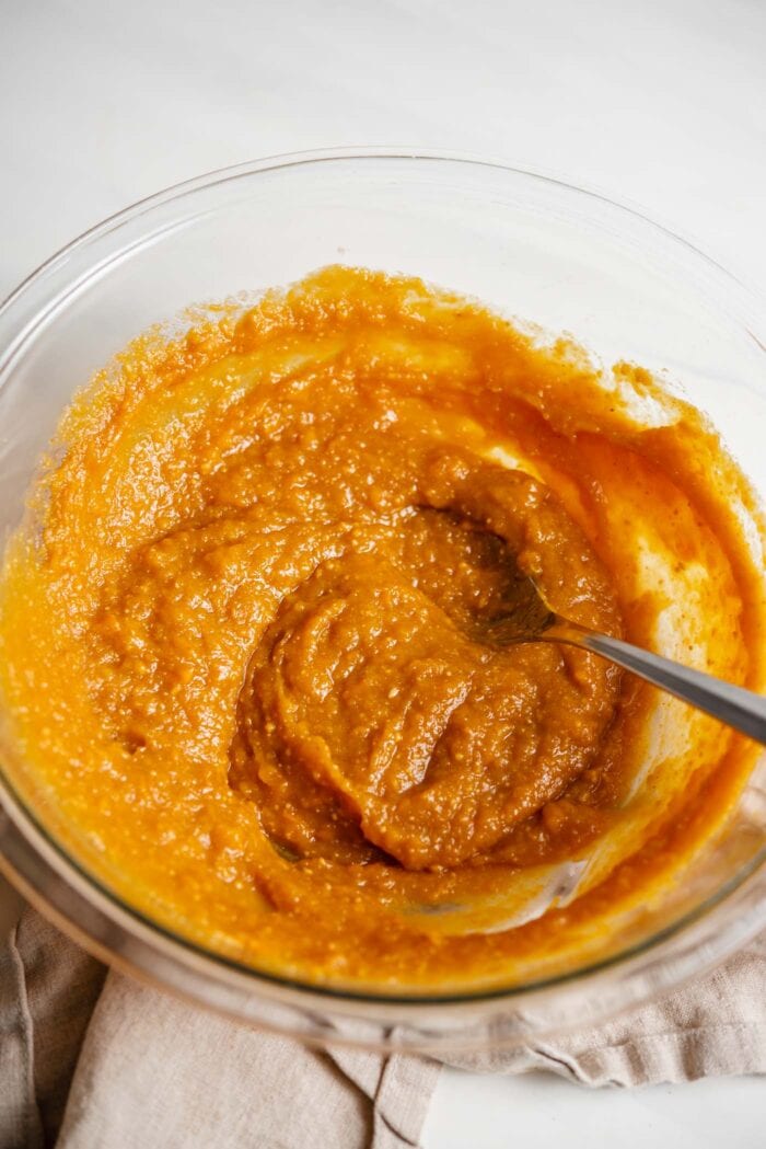A creamy sweet potato mixture in a glass mixing bowl with a spoon.