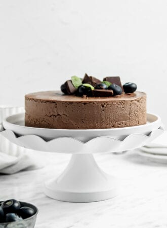 A chocolate cake topped with a few blueberries on a decorative cake stand.
